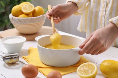 Photo of Woman cooking lemon curd at white wooden table, closeup