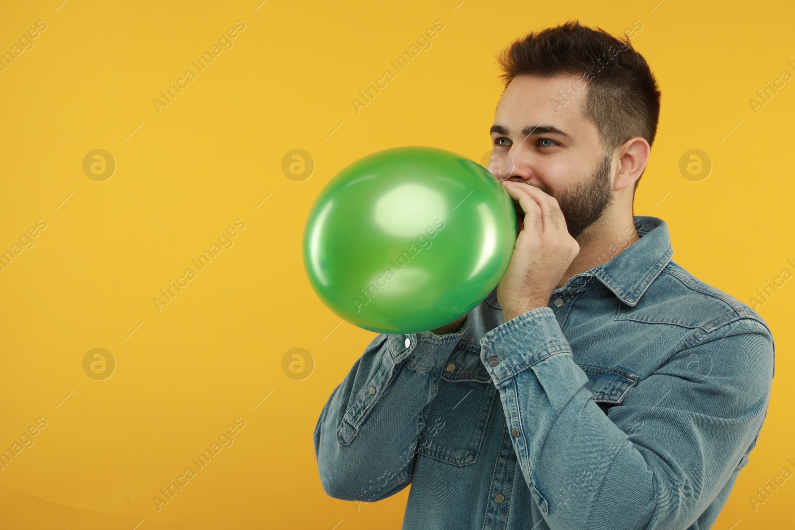 Photo of Man inflating bright balloon on yellow background, space for text