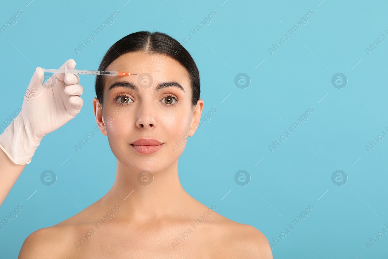 Photo of Doctor giving facial injection to young woman on light blue background, space for text. Cosmetic surgery