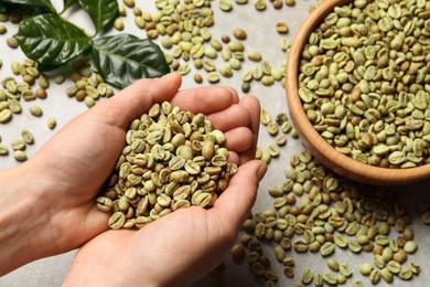 Photo of Woman holding pile of green coffee beans over grey table, top view