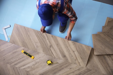 Photo of Worker installing laminated wooden floor indoors, above view