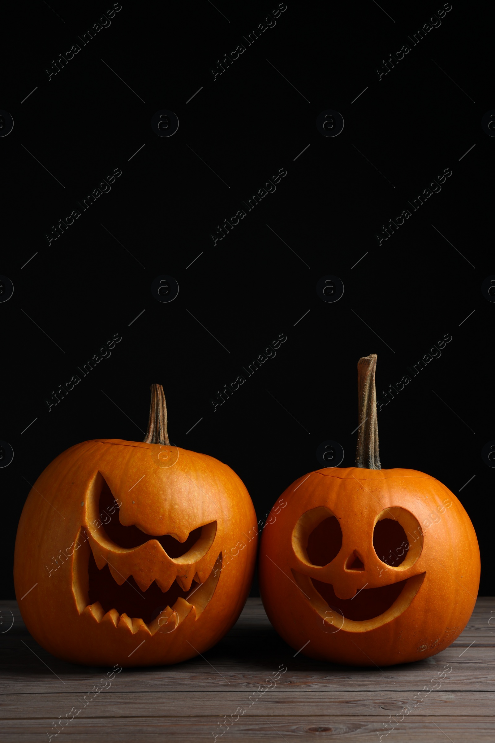 Photo of Scary jack o'lanterns made of pumpkins on wooden table against black background, space for text. Halloween traditional decor