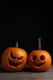 Scary jack o'lanterns made of pumpkins on wooden table against black background, space for text. Halloween traditional decor