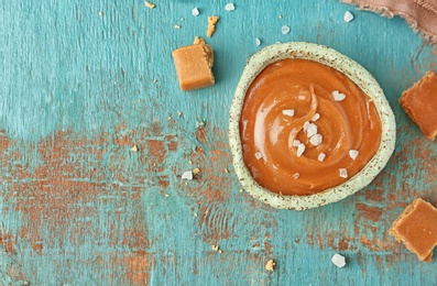 Photo of Delicious salted caramel sauce and candies on wooden background, top view