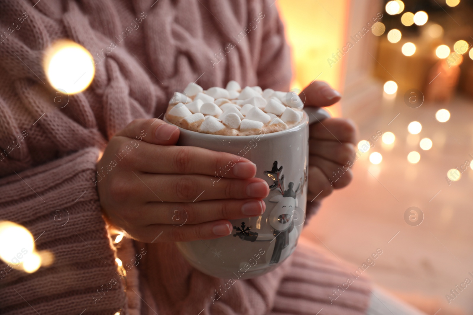 Photo of Woman holding cup of hot drink with marshmallows indoors, closeup. Magic Christmas atmosphere