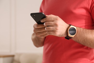 Young man with smart watch and phone at home, closeup. Space for text