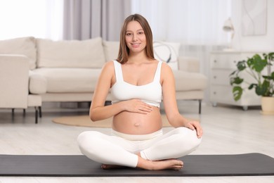 Beautiful pregnant woman sitting on yoga mat at home