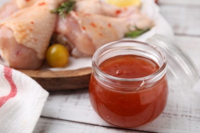 Marinade and raw chicken drumsticks on white wooden table, closeup