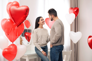 Photo of Lovely young couple in room decorated with heart shaped balloons. Valentine's day celebration