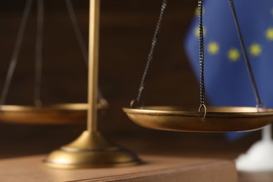 Photo of Scales of justice and European Union flag on wooden table, closeup