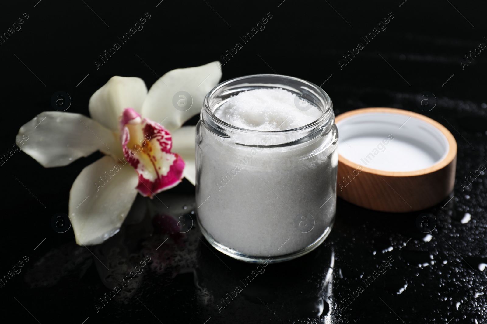 Photo of Jar with natural sea salt and beautiful flower on mirror table