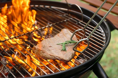 Photo of Tasty meat on barbecue grill with fire flames outdoors, closeup