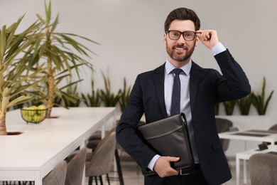 Photo of Happy real estate agent with leather portfolio indoors. Space for text