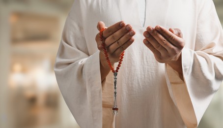 Muslim man with misbaha praying on blurred background, closeup. Banner design with space for text