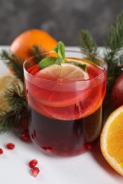 Photo of Christmas Sangria drink in glass, fir branches and fruits on white table, closeup