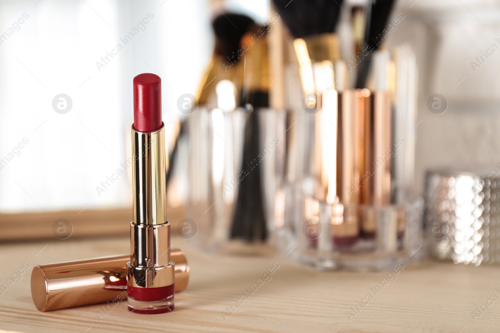 Photo of Bright lipstick in gold tube on dressing table, space for text