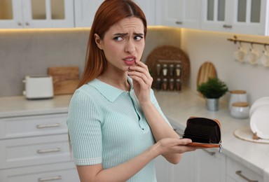Photo of Upset woman with empty wallet at home