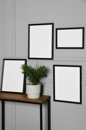 Photo of Empty frames hanging on grey wall near wooden table indoors