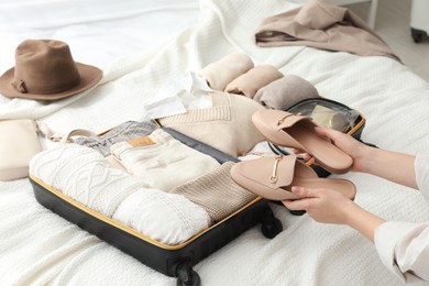 Photo of Woman holding fashionable shoes near open suitcase on bed, closeup