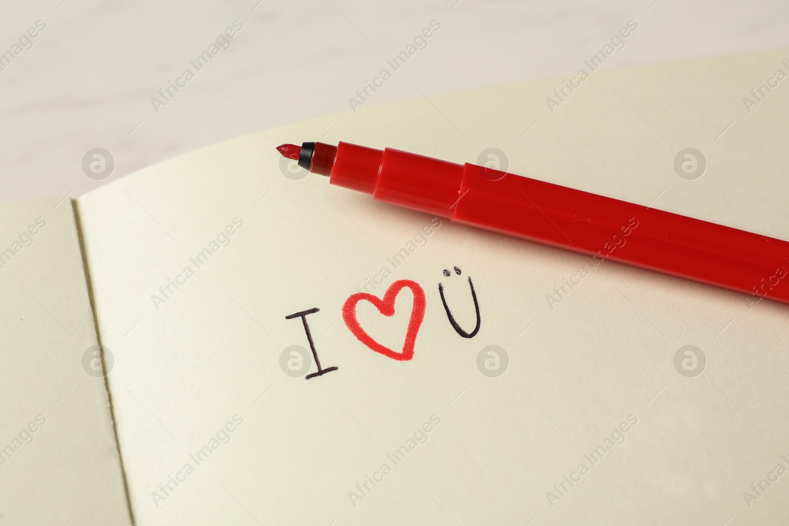 Photo of Notebook with text I Love You and red marker on white table, closeup