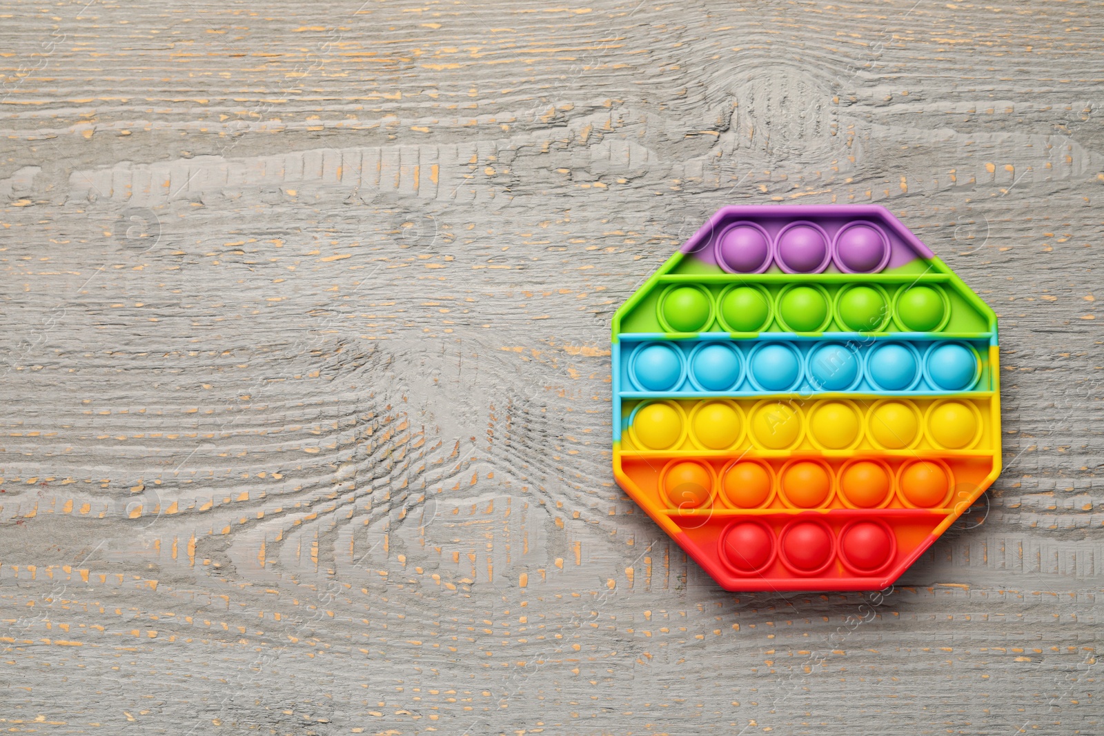 Photo of Rainbow pop it fidget toy on grey wooden table, top view. Space for text