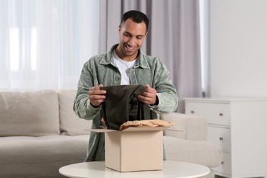 Photo of Happy young man opening parcel at home. Internet shopping