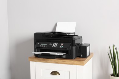 Modern printer with paper on chest of drawers indoors