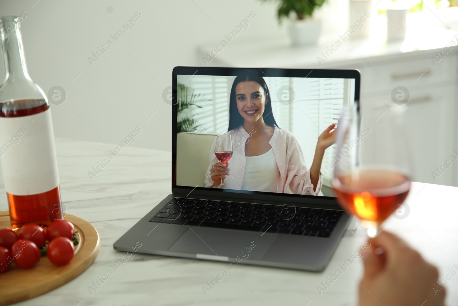 Photo of Friends drinking wine while communicating through online video conference in kitchen. Social distancing during coronavirus pandemic