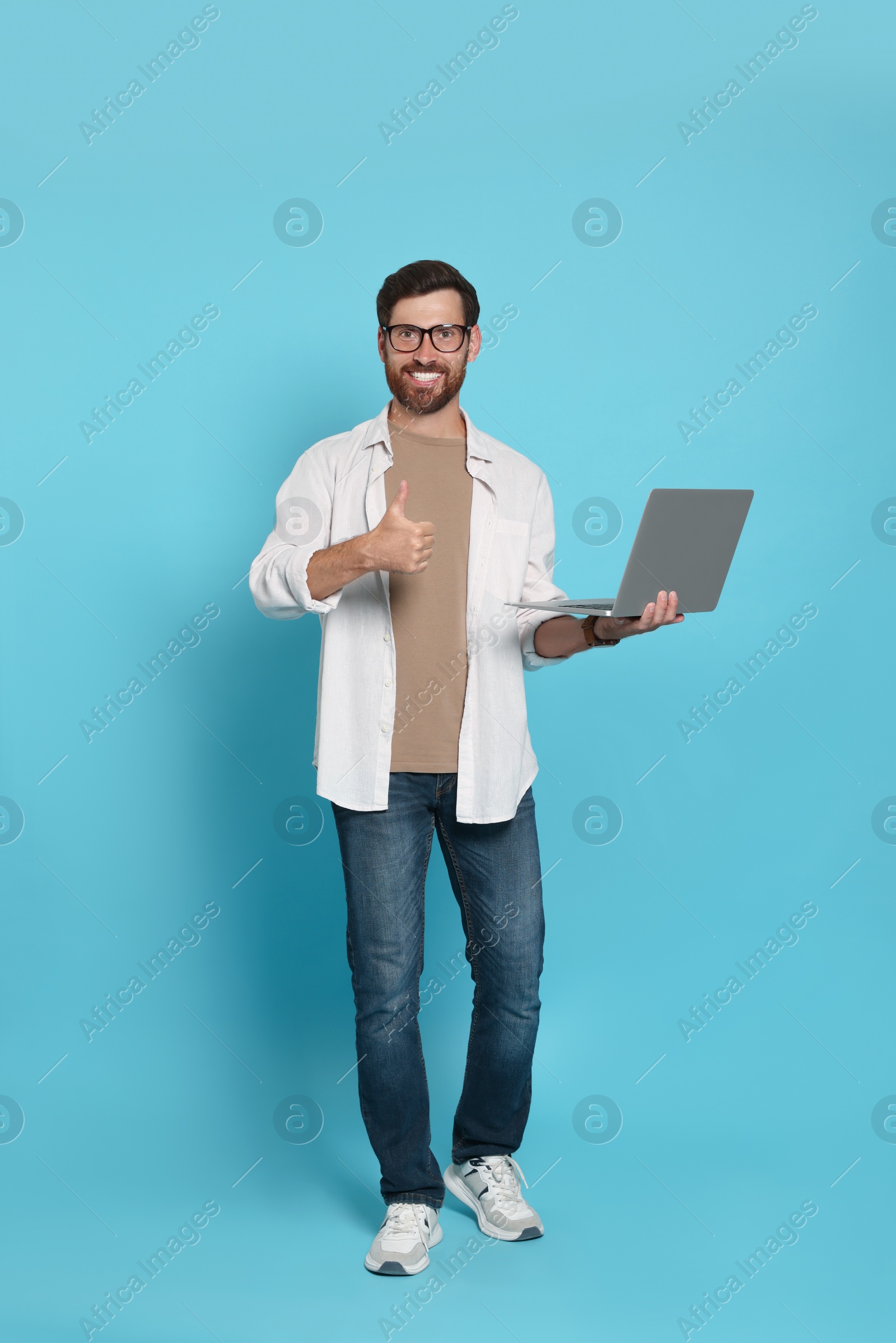 Photo of Handsome man with laptop showing thumb up gesture on light blue background