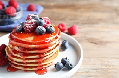 Delicious pancakes with fresh berries and syrup on wooden table. Space for text