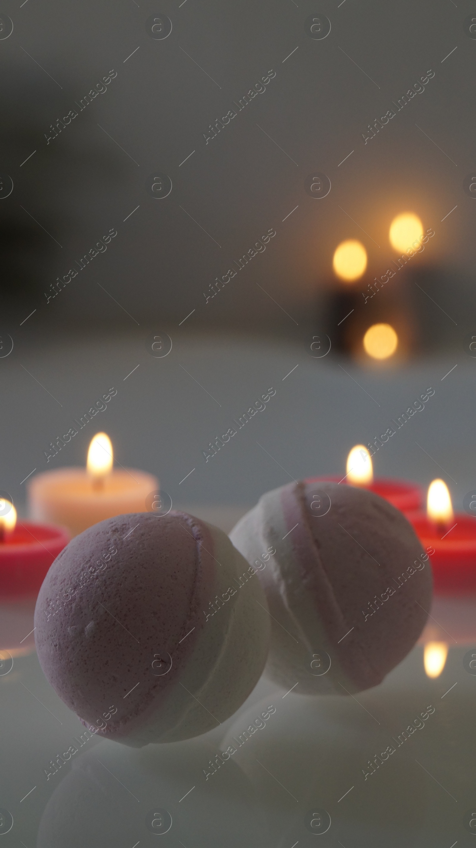 Photo of Bath bombs with burning candles on tub indoors. Bokeh effect