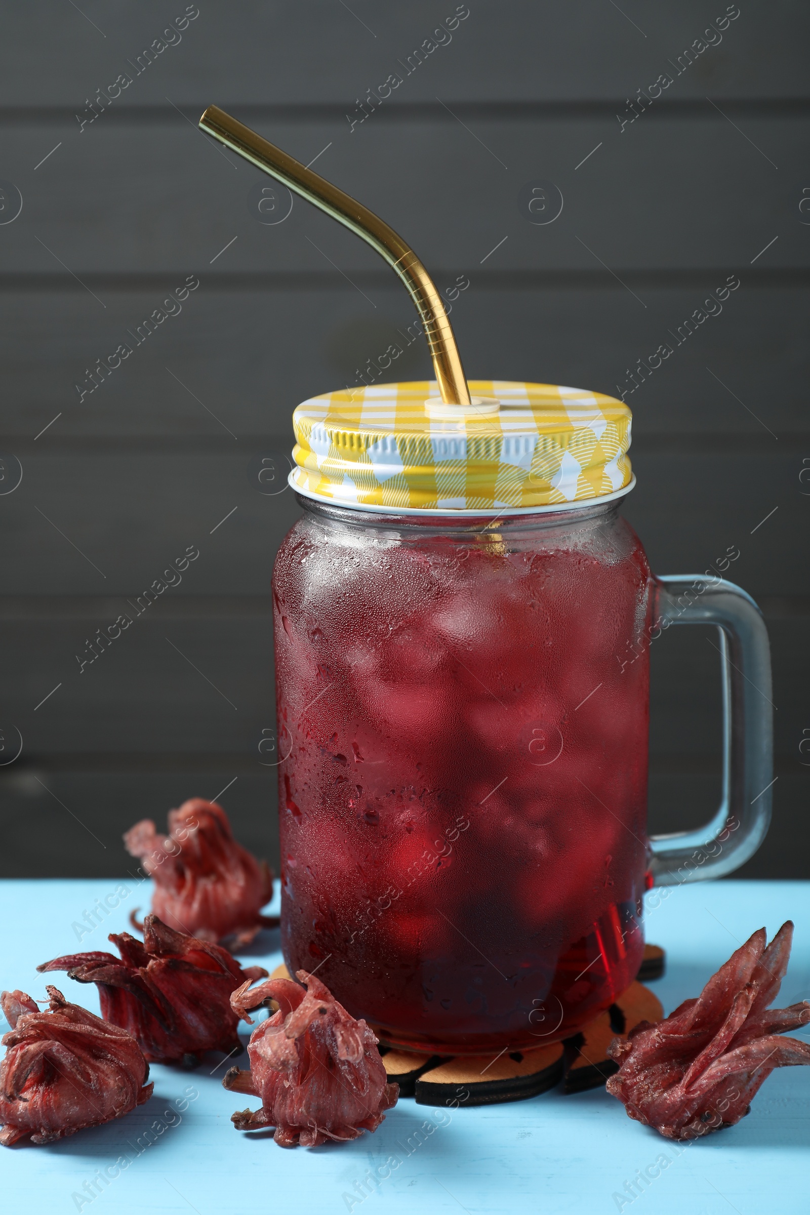 Photo of Mason jar of delicious iced hibiscus tea and dry flowers on light blue table
