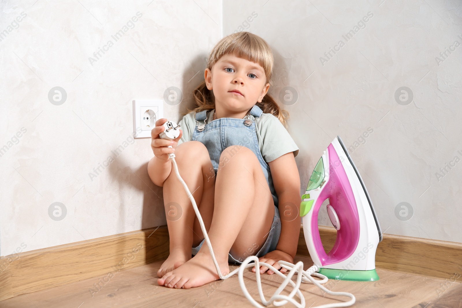 Photo of Little child playing with iron plug near electrical socket at home. Dangerous situation