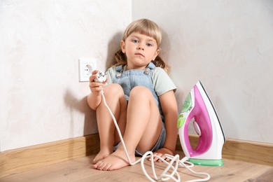 Photo of Little child playing with iron plug near electrical socket at home. Dangerous situation