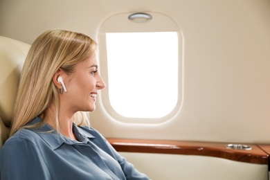 Image of Beautiful woman listening to music via wireless earphones during flight. Air travel