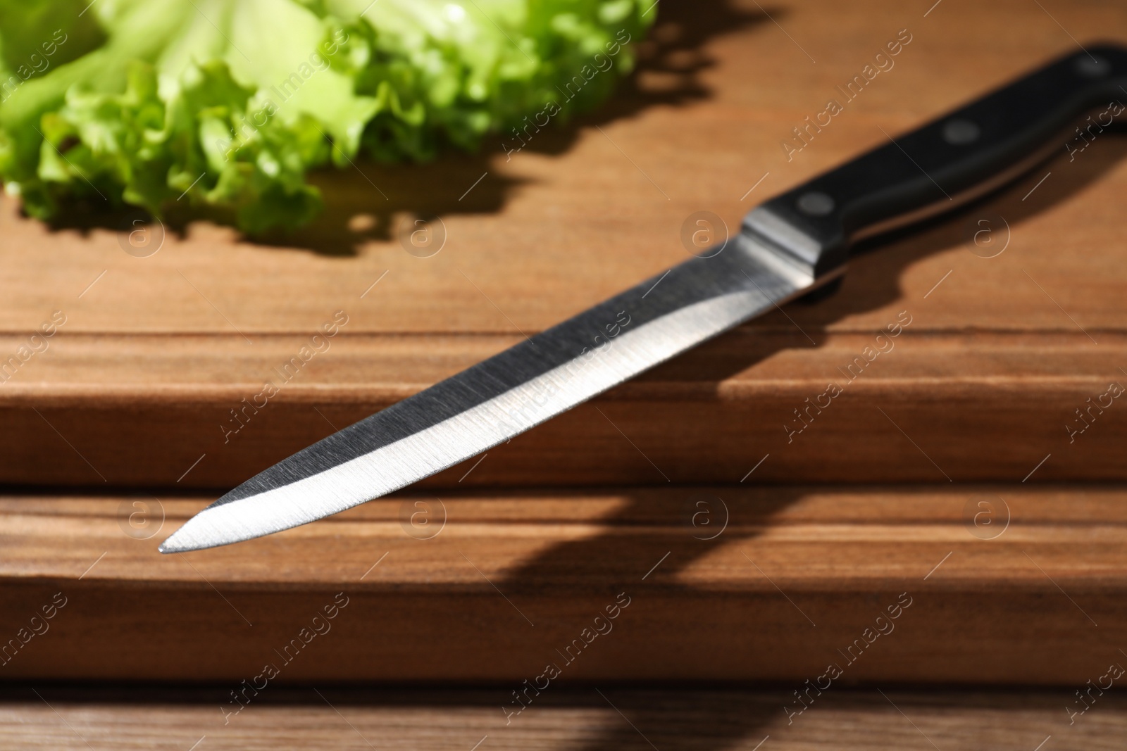 Photo of Utility knife and fresh lettuce leaves on wooden table, closeup. Clean dishes