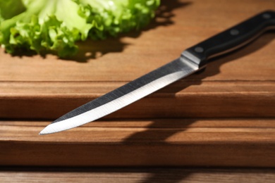 Utility knife and fresh lettuce leaves on wooden table, closeup. Clean dishes