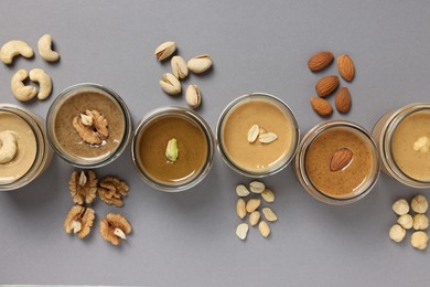 Tasty nut butters in jars and raw nuts on gray table, flat lay