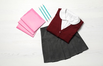 Photo of School uniform and stationery on white wooden background, top view