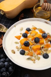 Photo of Bowl of delicious semolina pudding with blueberries, pumpkin and seeds on table, closeup