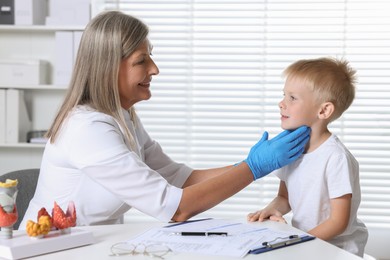 Endocrinologist examining boy's thyroid gland at table in hospital