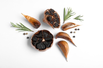 Aged black garlic with rosemary and peppercorns on white background, view from above