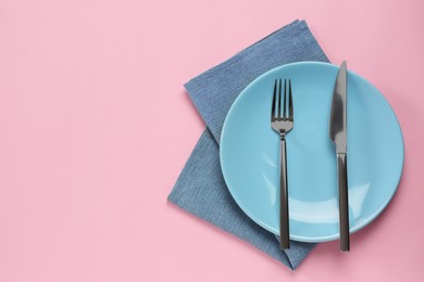 Clean plate with cutlery on pink background, flat lay. Space for text