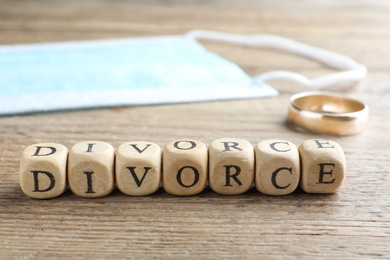 Cubes with word Divorce, protective mask and wedding ring on wooden table, closeup