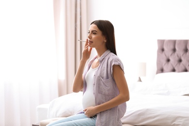 Photo of Young pregnant woman smoking cigarette at home