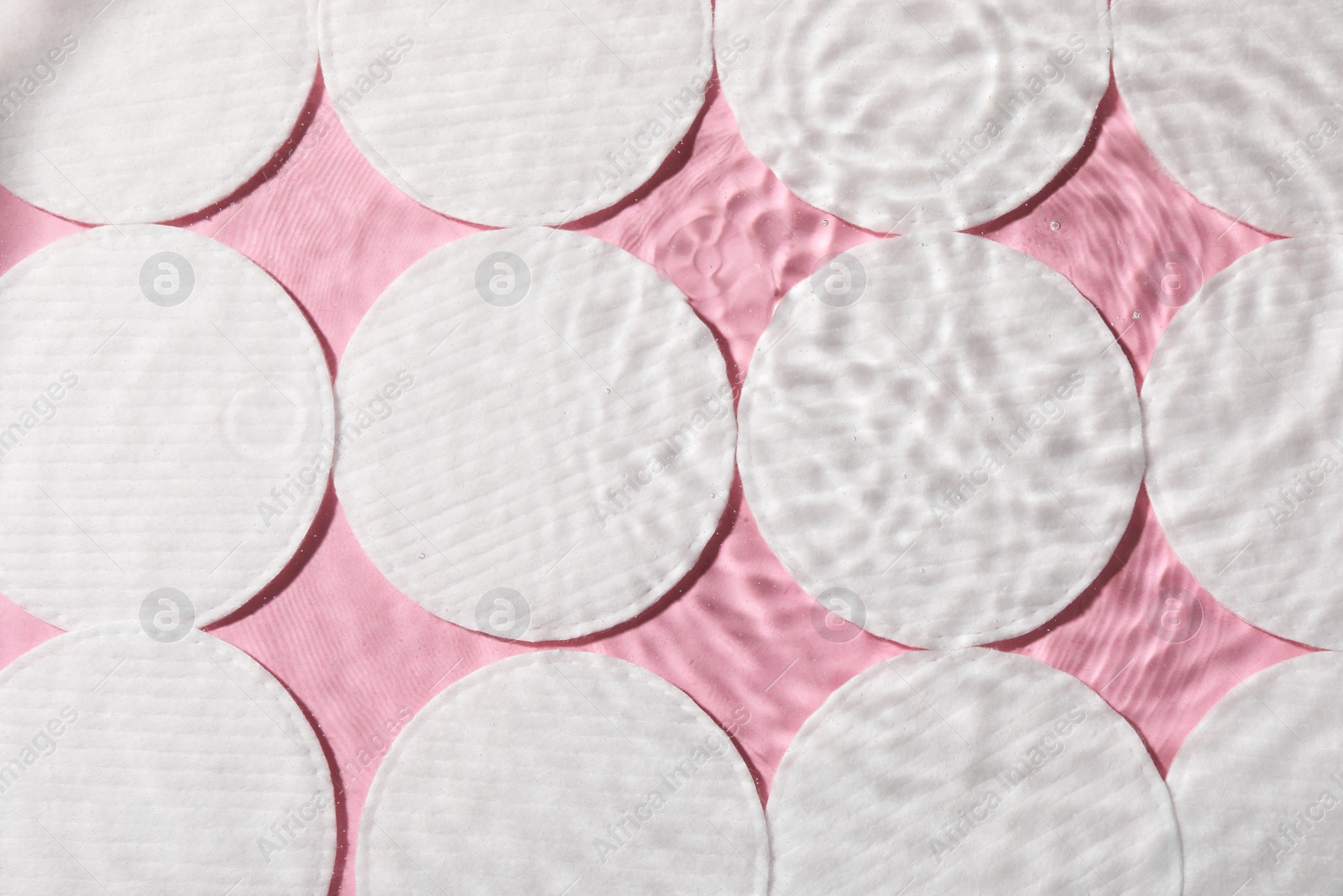 Photo of Many cotton pads in water on pink background, flat lay