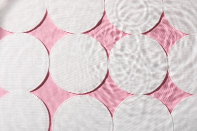 Many cotton pads in water on pink background, flat lay