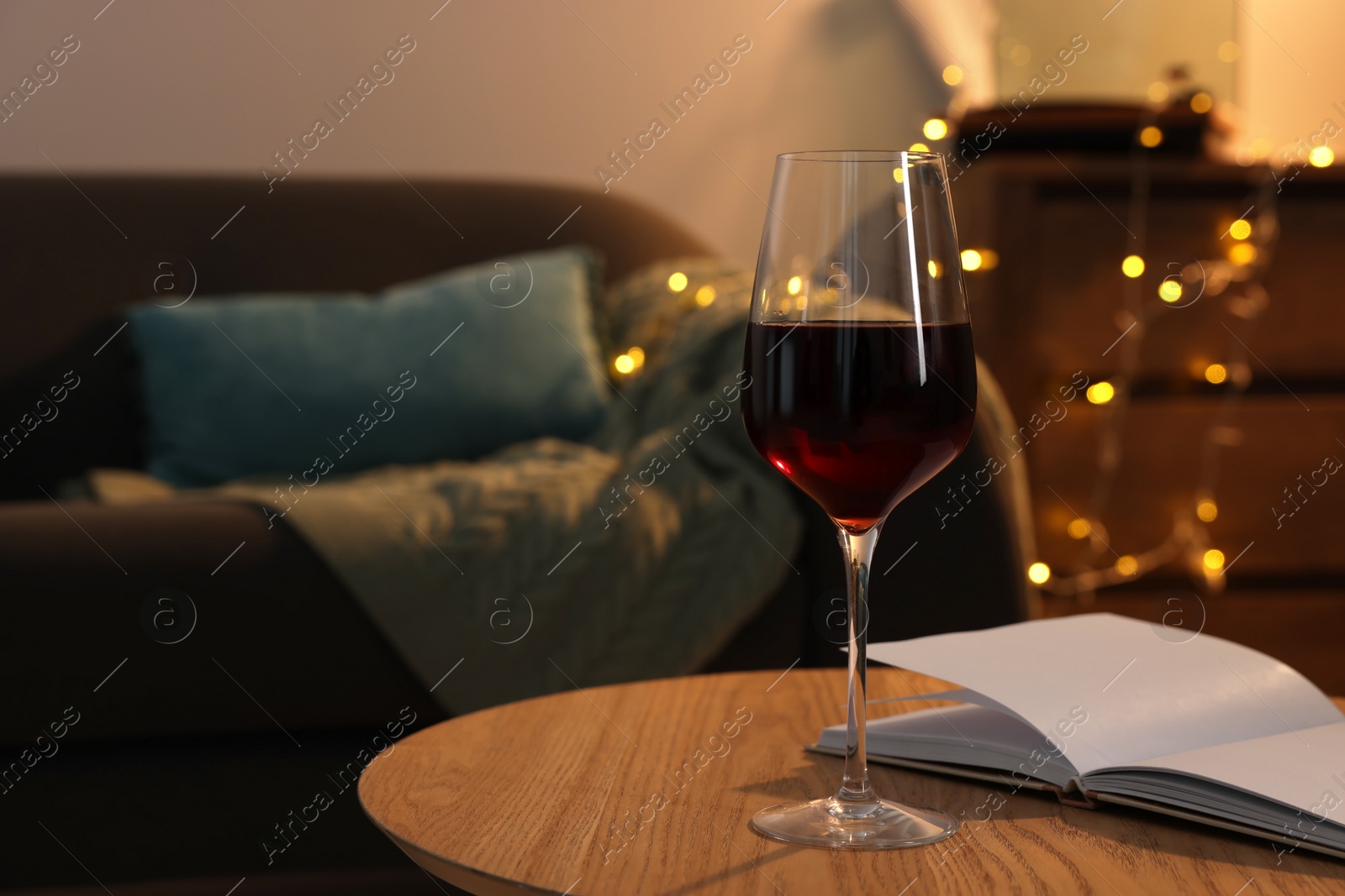 Photo of Glass of red wine and open notebook on wooden table in room, space for text. Relax at home