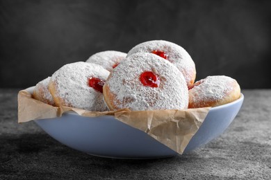 Delicious donuts with jelly and powdered sugar in bowl on grey table