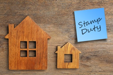 Image of House figures and sticky note with text Stamp Duty on wooden background, flat lay
